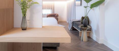 A modern bedroom with a wooden ceiling, a bedside table, a chair, a bed, a large plant, and a white round stool.