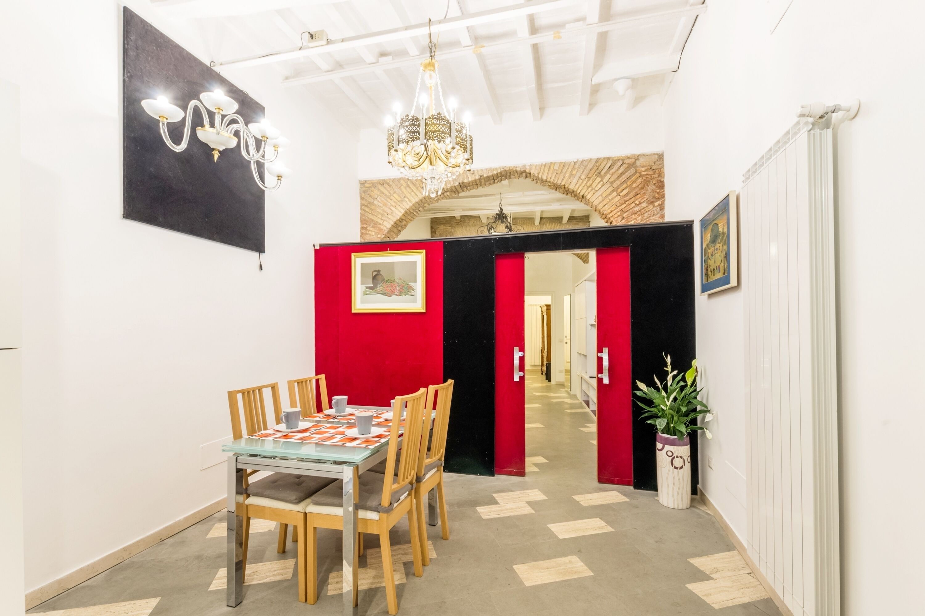 A dining area with a glass table, wooden chairs, a chandelier, and a red partition.