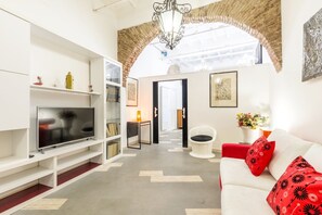 A modern living room with a flat-screen TV, white sofa, red cushions, a white chair, and a decorative lamp. - Navona Harmony Apartment - Spagnoli (Rome)