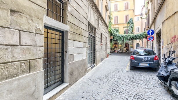 A narrow cobblestone street with a parked car and a scooter, flanked by historic buildings with barred windows and a no parking sign. - Navona Harmony Apartment - Spagnoli (Rome)