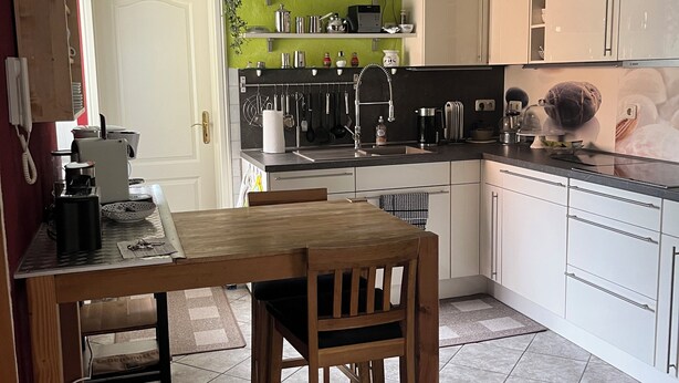 Una cocina con una mesa y sillas de madera, una cafetera y diversos utensilios de cocina.