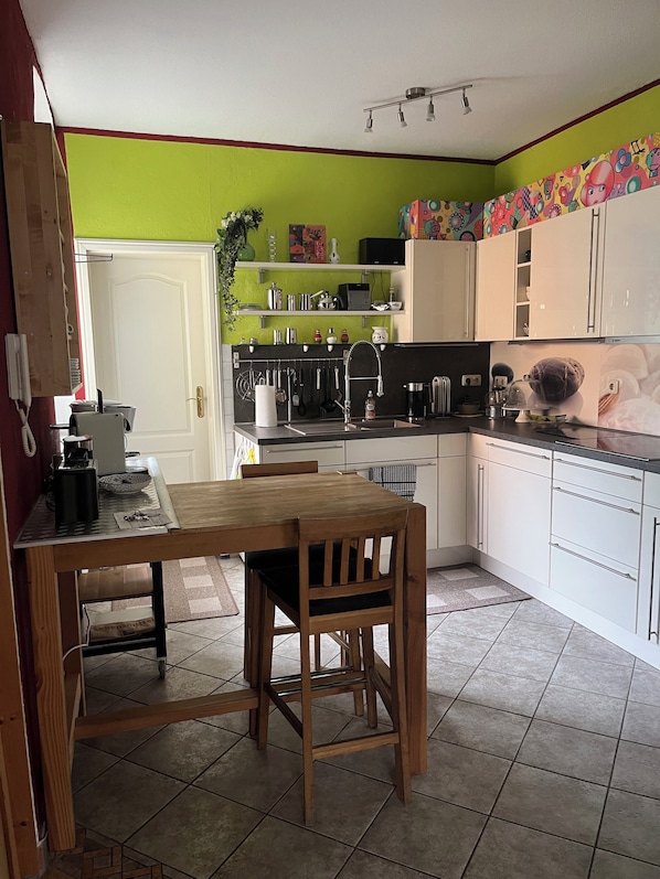 A kitchen with a wooden table and chairs, a coffee machine, and various kitchen utensils.