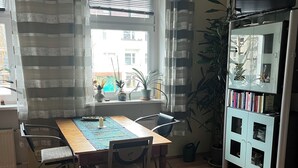 Un comedor con una mesa de madera, sillas de metal, un camino de mesa a rayas y una estantería llena de libros.