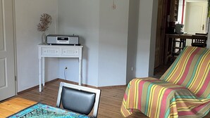 Una sala de estar con una mesa de madera, un sofá a rayas, un escritorio blanco y un cuadro en la pared.