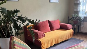 Una habitación con un sofá, una planta en maceta, un cuadro en la pared y una ventana con cortinas.