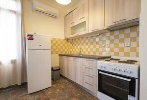 Een koelkast, een oven, een kookplaat, kookgerei, borden en bestek