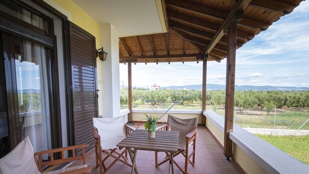 Um alpendre coberto com mesa e cadeiras, vista para um vinhedo e um edifício ao longe.