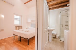 A bedroom with a bed, a window, a radiator, and a bathroom with a shower and sink. - La Casetta-Stazione Verona Porta Vescovo (Verona)