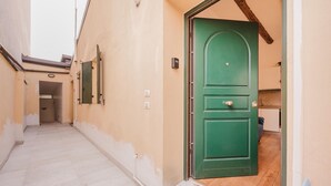 Un corridoio stretto con una porta verde che dà su una stanza con pavimento in legno e termosifone.