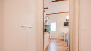 Un corridoio che conduce a una cucina con una finestra, un tavolo bianco e una sedia blu.