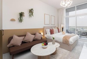 Ein modernes Hotelzimmer mit einer Couch, einem Bett, einem runden Tisch mit Früchten und Blick auf die Stadt.