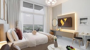Una habitación de hotel moderna con cama, una mesa de comedor redonda, una pequeña cocina y un gran ventanal con vistas a la ciudad.