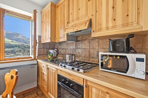 A kitchen with wooden cabinets, a gas stove, a microwave, and a window with a view of hills.