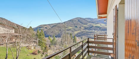 A balcony with a view of a mountainous landscape, a wooden railing, and a building with a sloped roof.