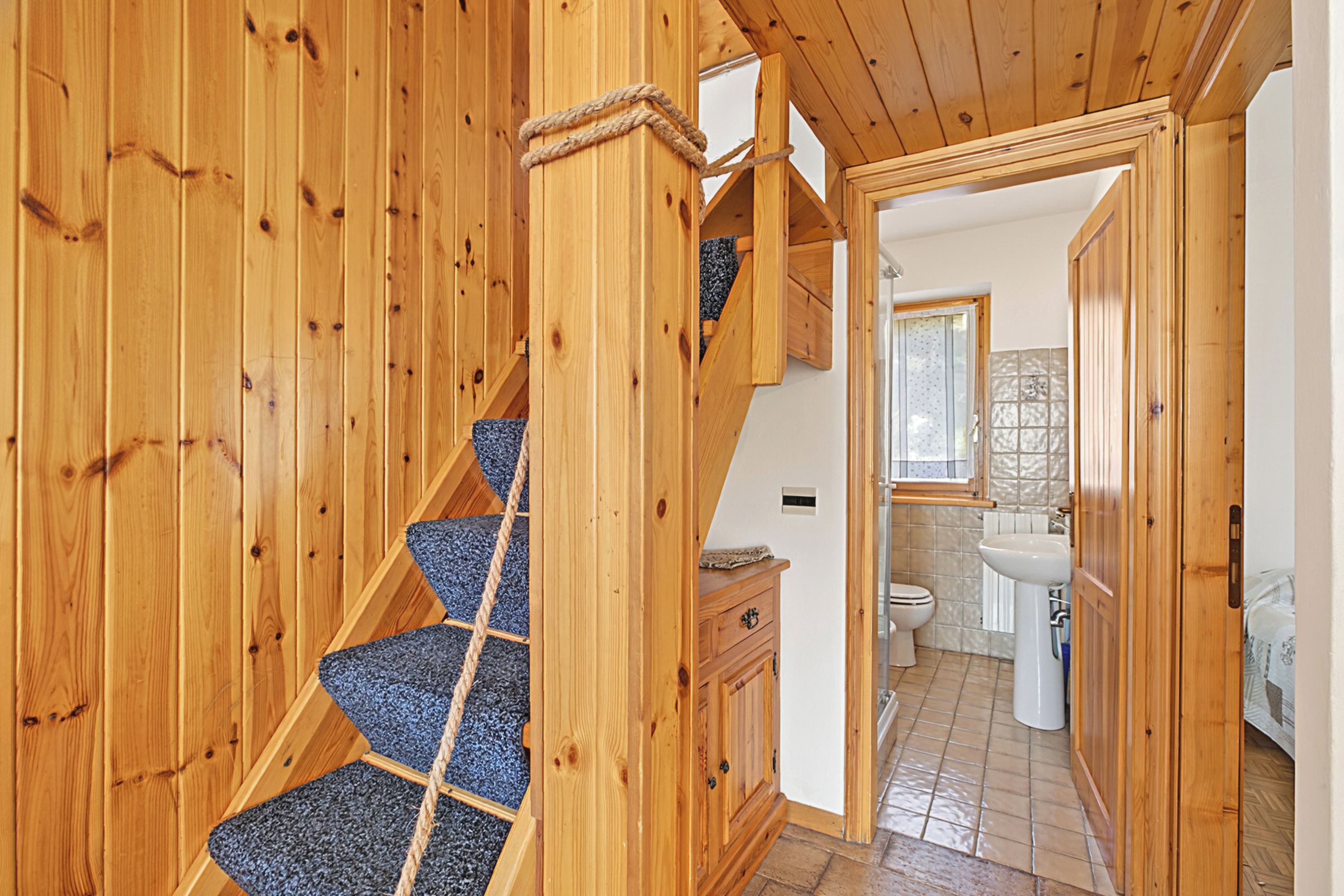 Un escalier en bois mène à une chambre dont le plafond est également en bois et qui offre une vue sur la salle de bain.