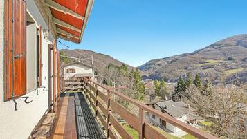 Ein Balkon mit Blick auf eine gebirgige Landschaft, einem Holgitter und einem Gebäude mit schrägem Dach.