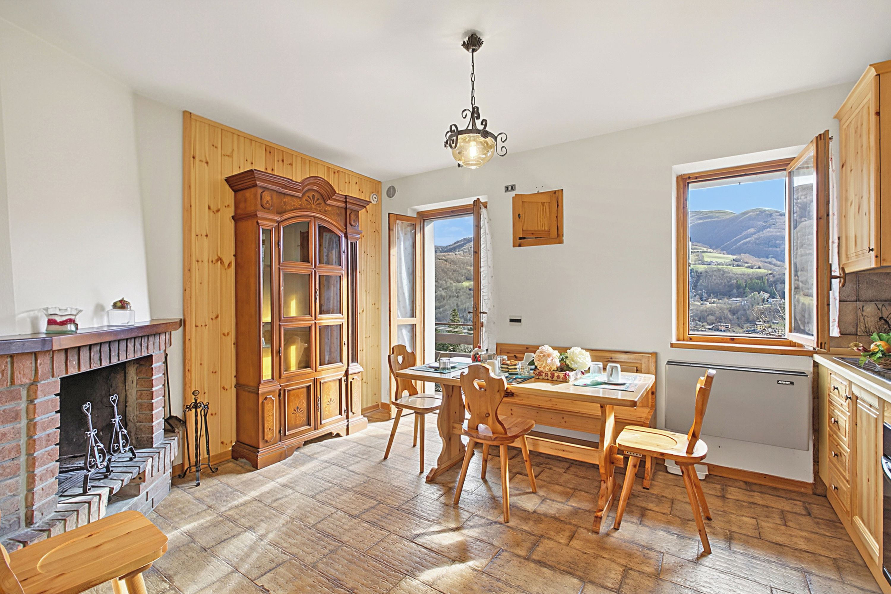 A kitchen with wooden cabinets, a dining table, chairs, a fireplace, and a view of the outdoors.