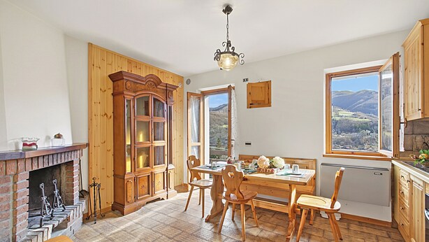 A kitchen with wooden cabinets, a dining table, chairs, a fireplace, and a view of the outdoors. - Casa Maria - Mountain Sports Base (Pievepelago)