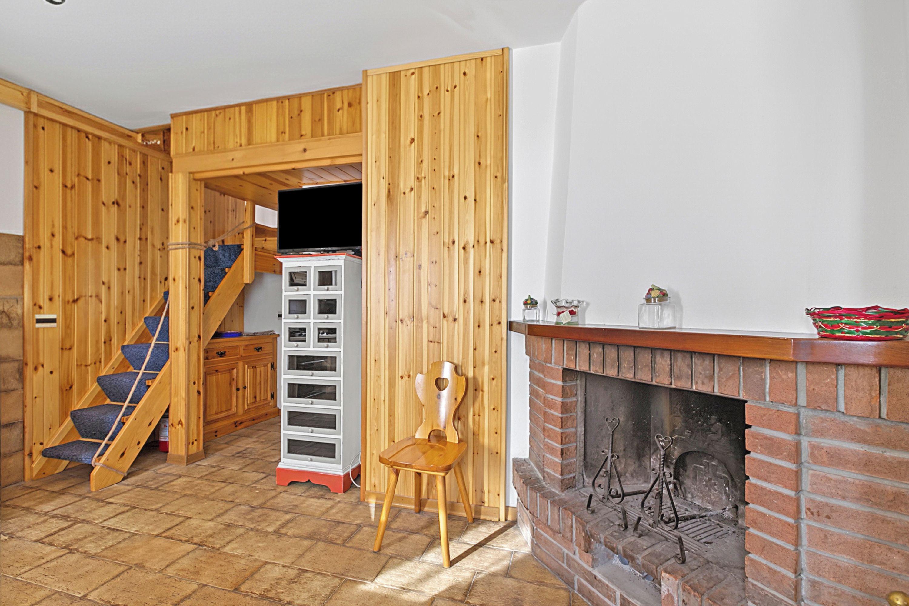 Un intérieur en bois avec une cheminée, une chaise en bois, un escalier et un meuble blanc.