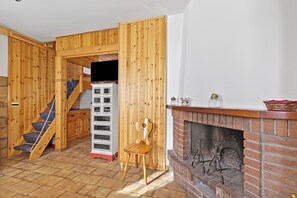 A wooden interior with a fireplace, a wooden chair, a staircase, and a white cabinet.
