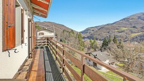 A balcony with a view of a mountainous landscape, a wooden railing, and a building with a sloped roof. - Casa Maria - Mountain Sports Base (Pievepelago)