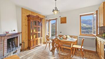 Une cuisine avec des meubles en bois, une table à manger, des chaises, une cheminée et une vue sur l’extérieur.