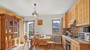 A kitchen with wooden cabinets, a dining table with chairs, a stove, and a microwave. - Casa Maria - Mountain Sports Base (Pievepelago)