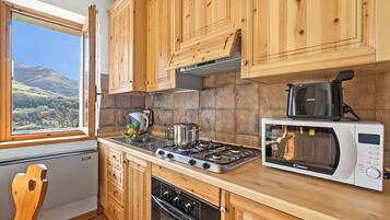 Una cocina con armarios de madera, estufa a gas, microondas y ventana con vistas a las colinas.