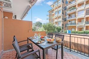 Un balcón con mesa lista para una comida, rodeado por una baranda de metal, con vista a un edificio residencial.