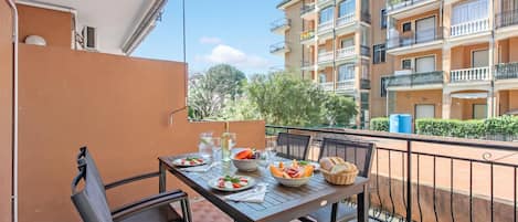 A balcony with a table set for a meal, surrounded by a metal railing, and overlooking a residential building.