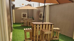 A patio area with a wooden table and chairs, an umbrella, and artificial grass.