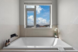 Een moderne badkamer met een badkuip, een raam met uitzicht op de stad en een potorkidee.