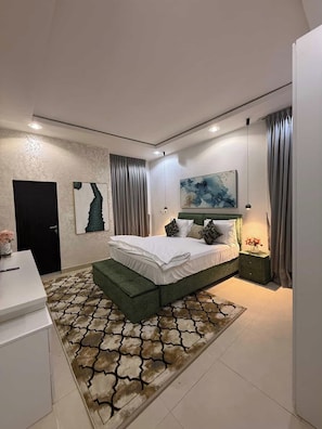 A modern bedroom with a green bed, a white bedside table, and a patterned rug.