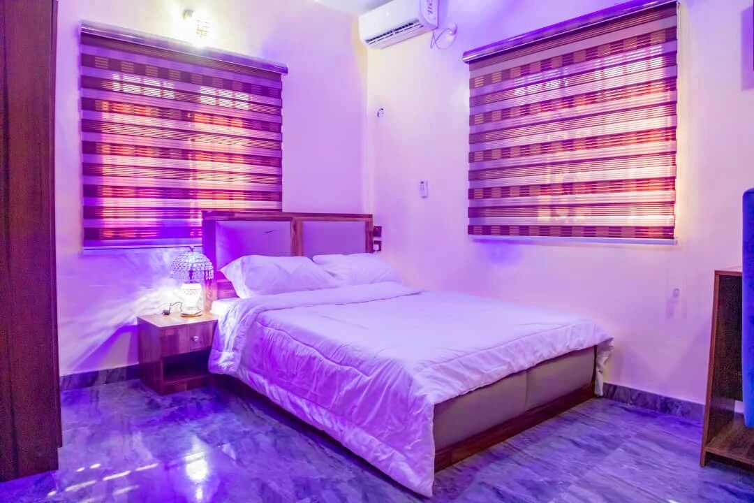 A bedroom with a bed, nightstand, and window blinds.
