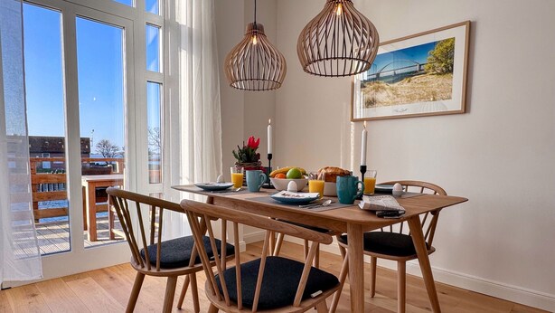 Een eetgedeelte met een houten tafel, stoelen, een kaars, ontbijtartikelen en een lijst aan de muur.