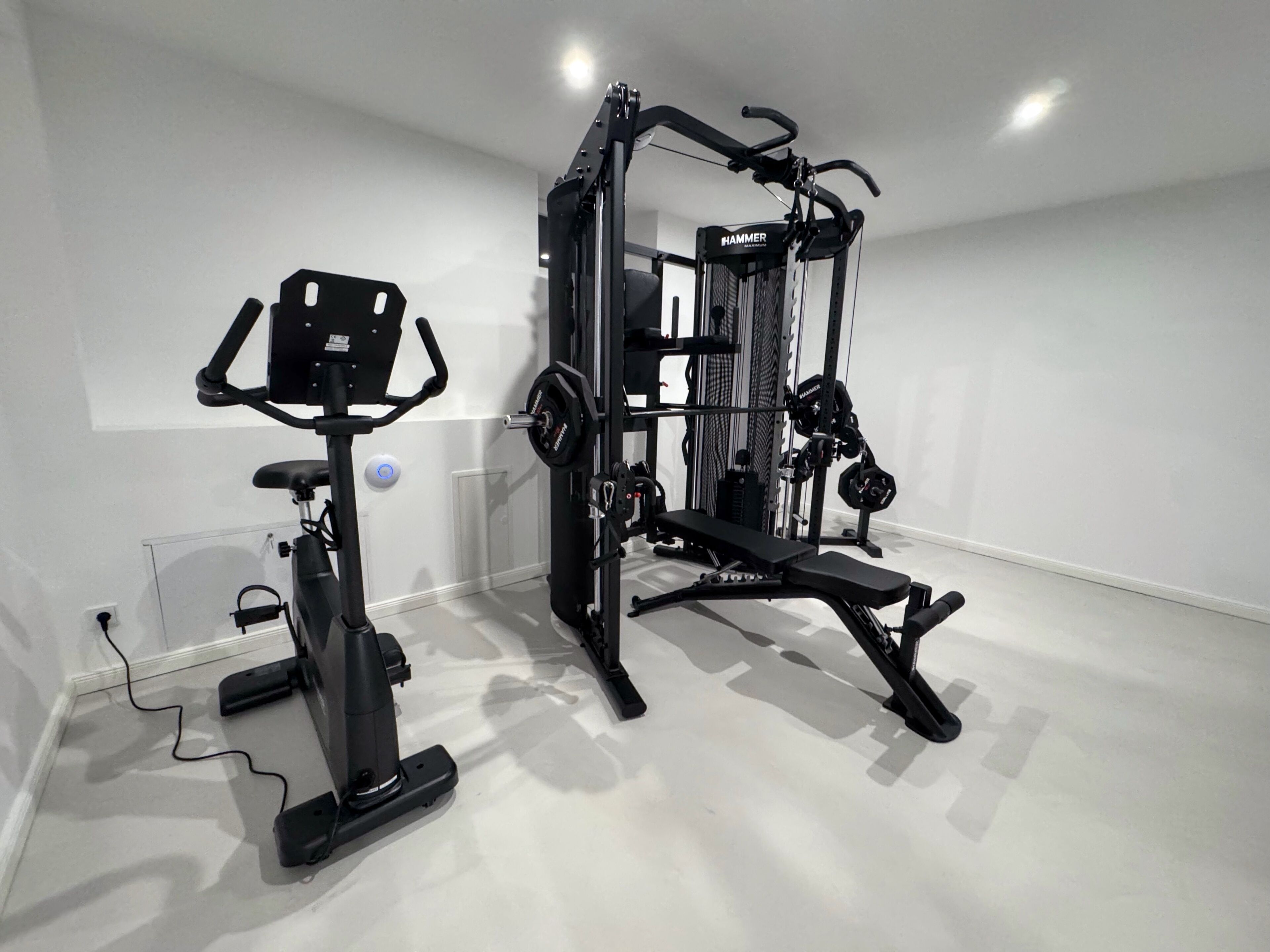 A gym with a stationary bike, a multi-functional workout station, and a bench.