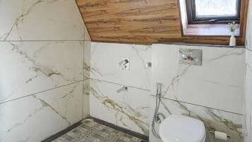 A bathroom with a wooden ceiling, a window, a toilet, and patterned floor tiles.