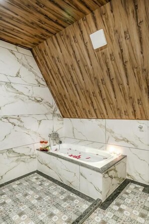A bathroom with a wooden ceiling, marble walls, and a bathtub with rose petals. - The Bagh Kufri (Theog)