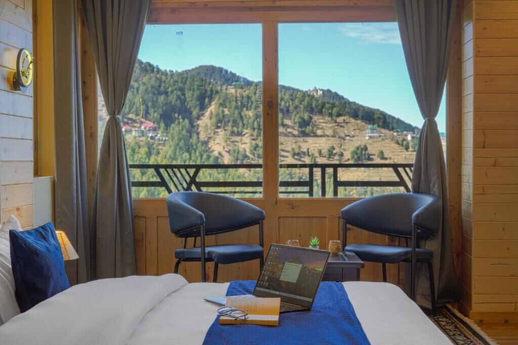 A bedroom with a bed, a laptop, and two chairs.
