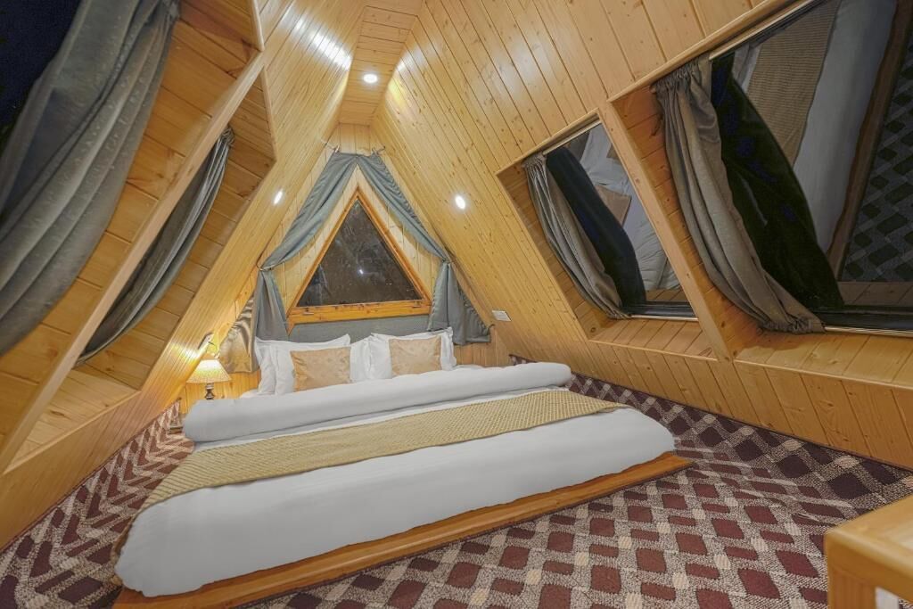 Een zolderkamer met een driehoekige vorm, een bed, een raam en een lamp.