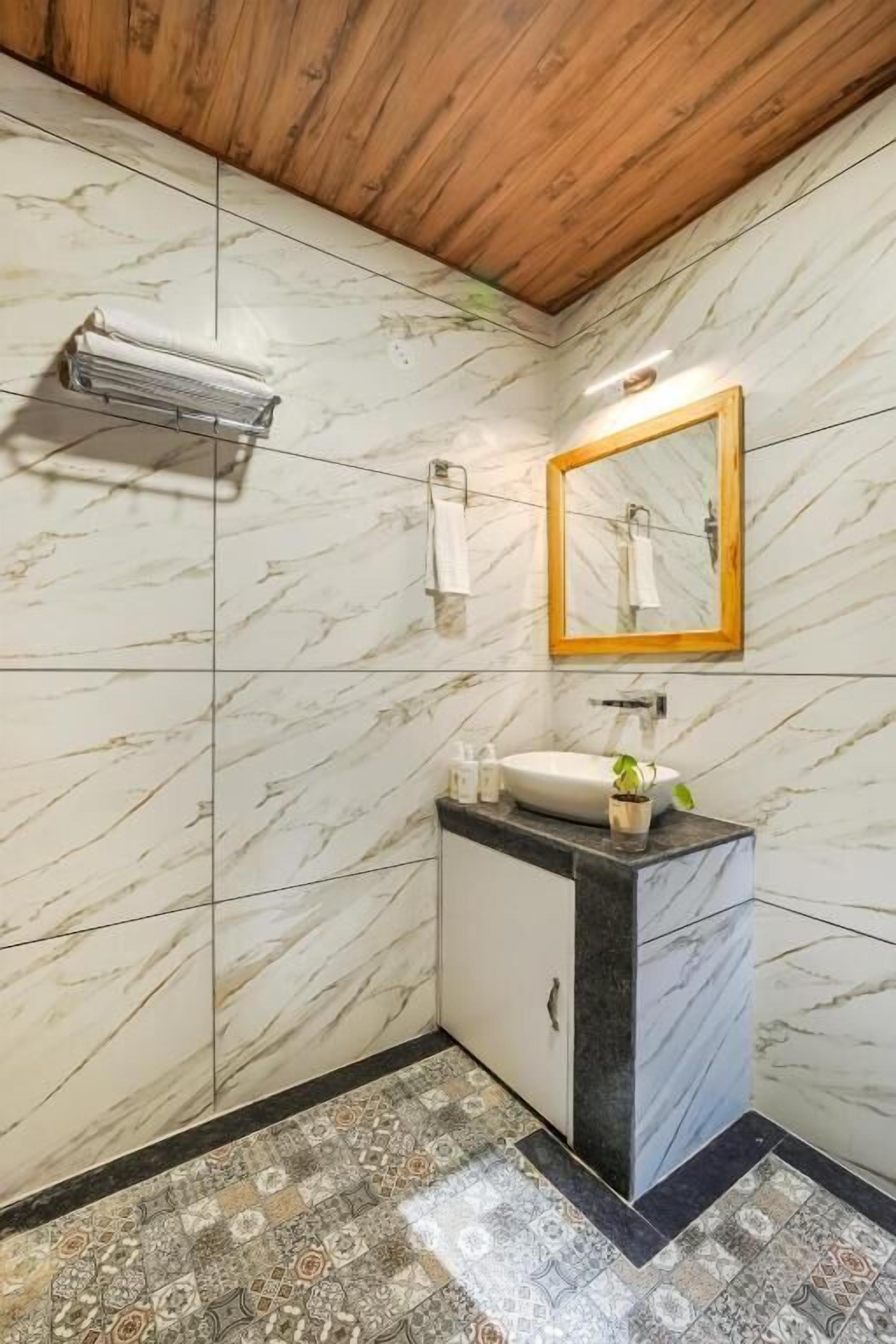 A bathroom with marble walls, a wooden ceiling, a sink with a mirror, and patterned floor tiles.