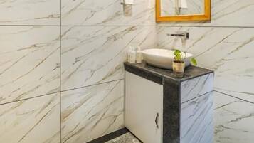 A bathroom with marble walls, a wooden ceiling, a sink with a mirror, and patterned floor tiles.