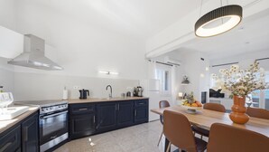 Et moderne køkken med en central ø, sorte skabe, stålstål-hvidevarer og et spiseområde med et træbord og stole.