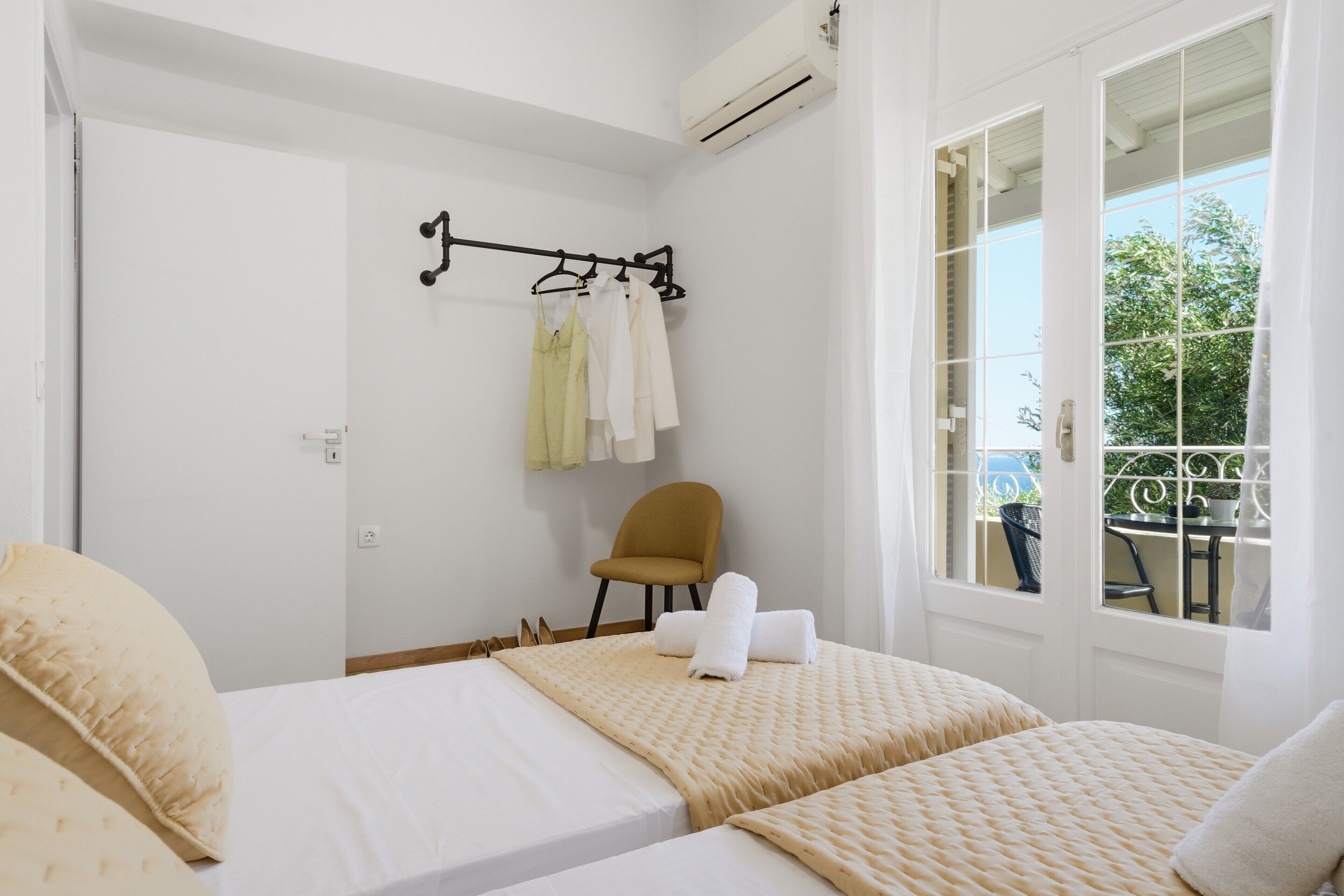 Une chambre d’hôtel avec deux lits, une chaise, une fenêtre donnant sur un paysage agréable et un porte-vêtements avec des vêtements suspendus.