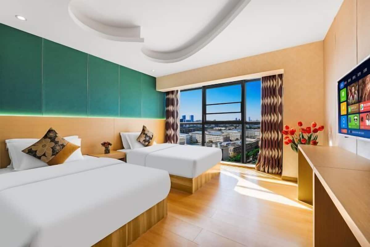 Habitación de hotel con dos camas, un ventanal amplio con vista a la ciudad y un televisor de pantalla plana en la pared.
