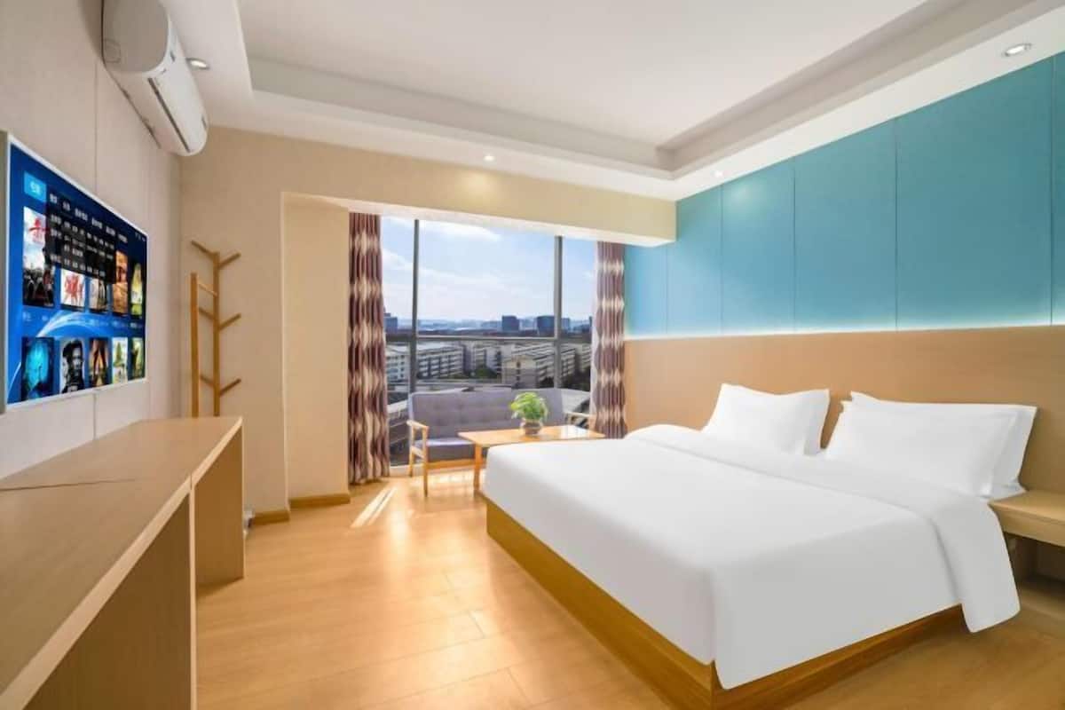 Habitación de hotel con una cama grande, un escritorio, un televisor y vistas a la ciudad.