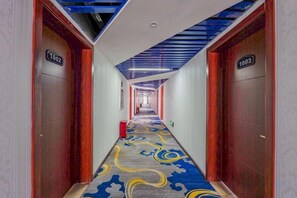 Ein Hotelgang mit Teppichmuster, Holztüren und blauer Decke.