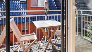 Un balcone con un tavolo e due sedie di legno, un muro in mattoni rossi e un tetto con tegole blu.
