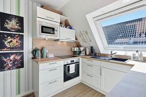 Eine moderne Küche mit weißen Schränken, einer Mikrowelle, einem Wasserkocher und einem Fenster mit Blick auf ein Ziegeldach.