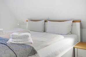 Una habitación de hotel con una cama, almohadas, una mesita de noche y una lámpara.